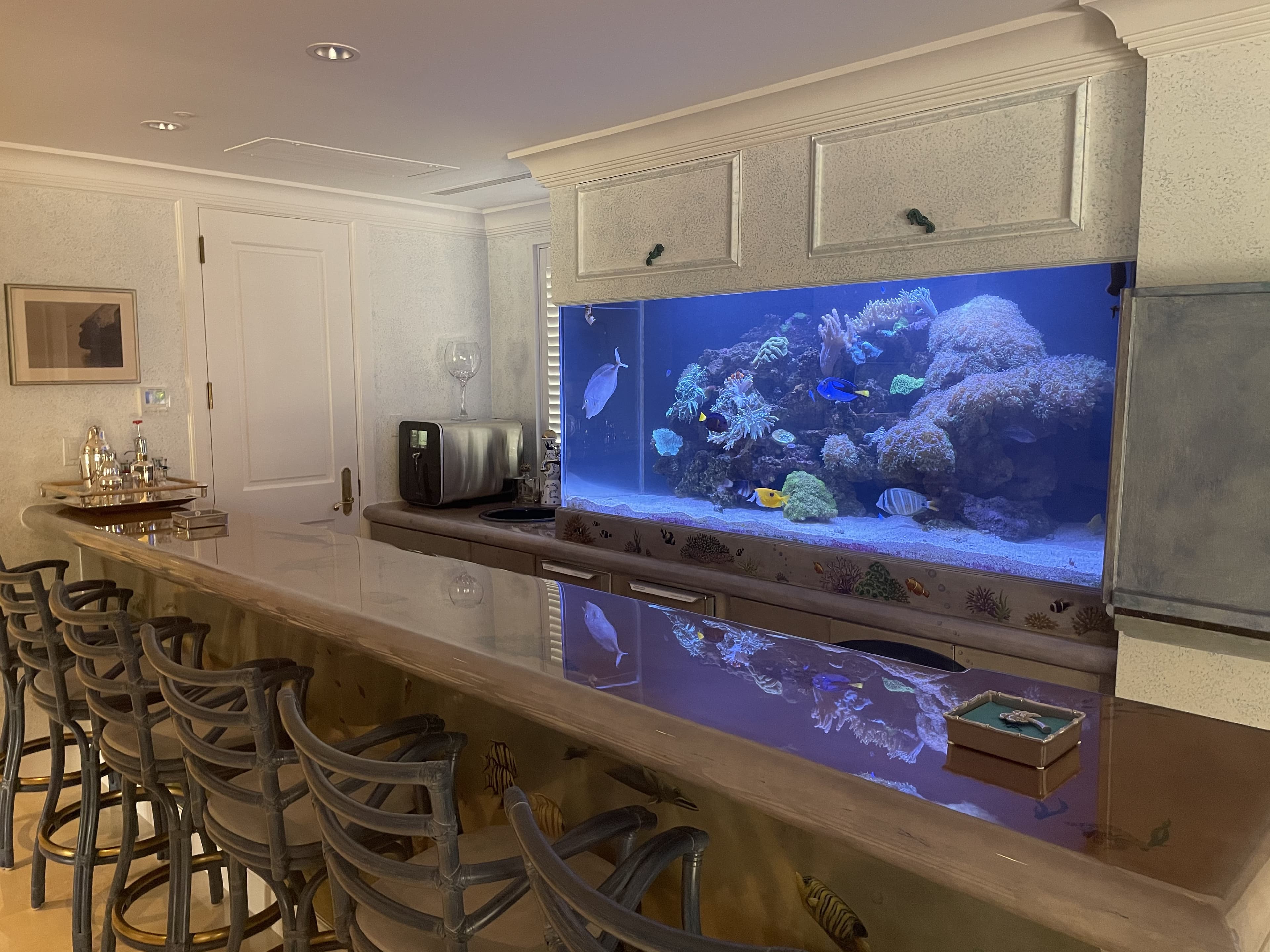Luxury reef aquarium built into a home bar with barstools, custom installation by Aquaholic Aquarium Services in Palm Beach County